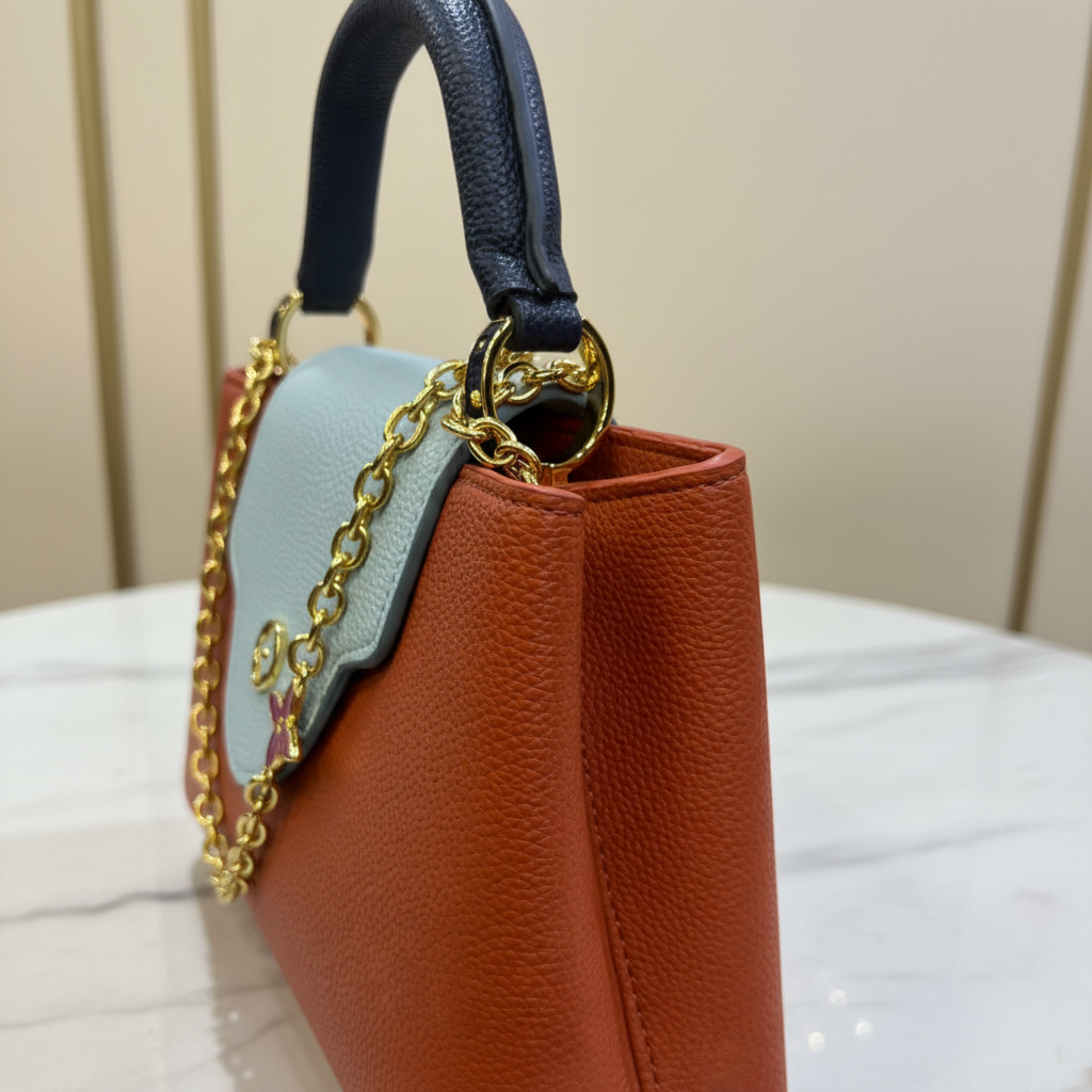 Louis Vuitton Capucines Orange Rust side hardware detail on white marble