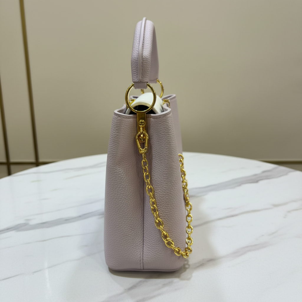 Louis Vuitton Capucines Blush Pink side handle hardware detail on white marble